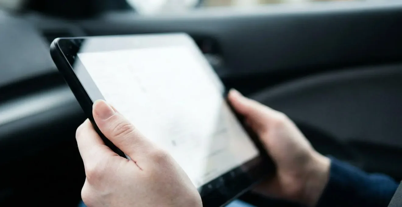 Hands holding tablet during outdoor vehicle walk-around with car body panel visible in background