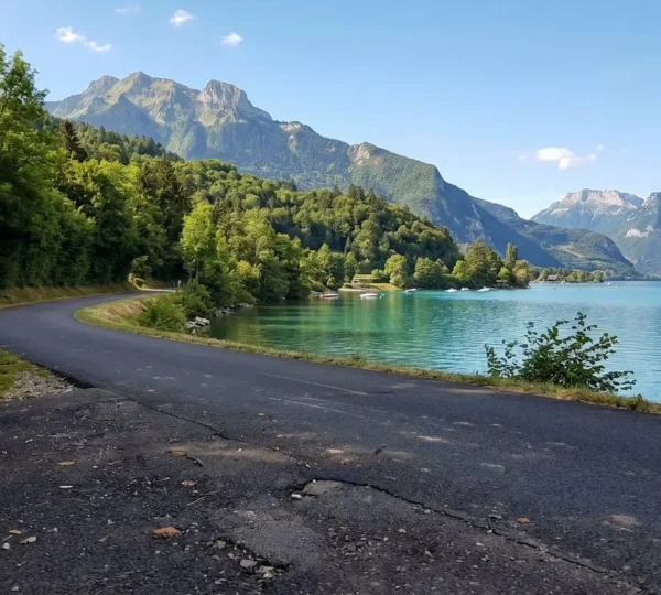 Dedicated cycling path curving alongside Lake Annecy's turquoise waters with distant Alpine peaks